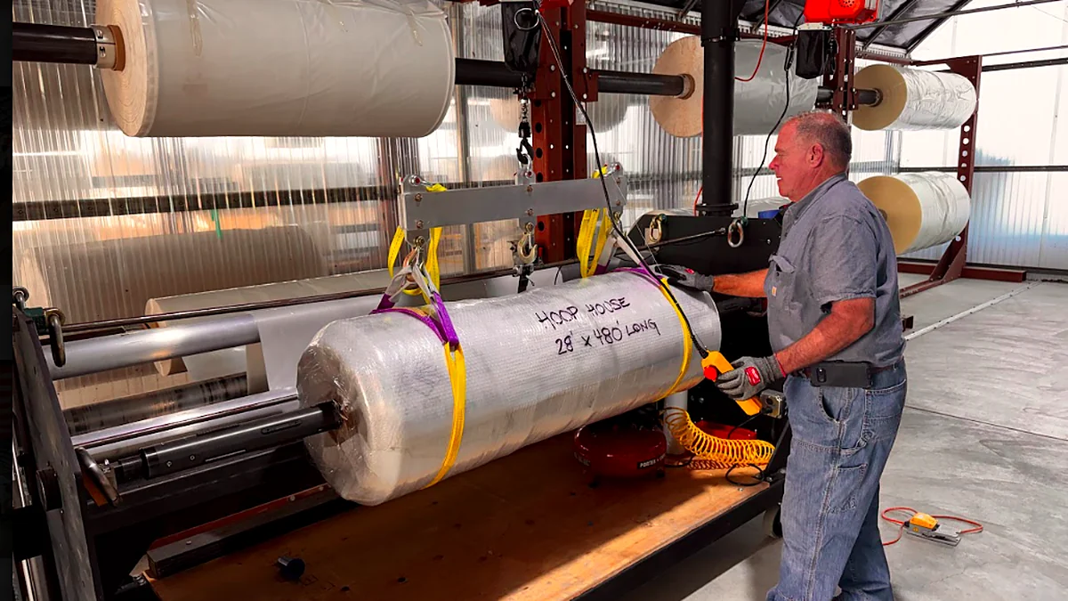 Ferrari Metals employee handling a custom greenhouse film roll on in-house cutting and rewinding equipment