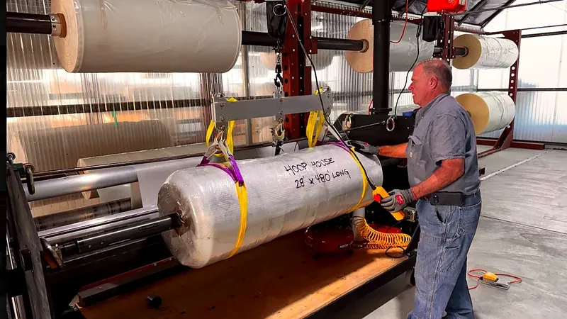 Ferrari Metals employee handling a custom greenhouse film roll on cutting and rewinding equipment